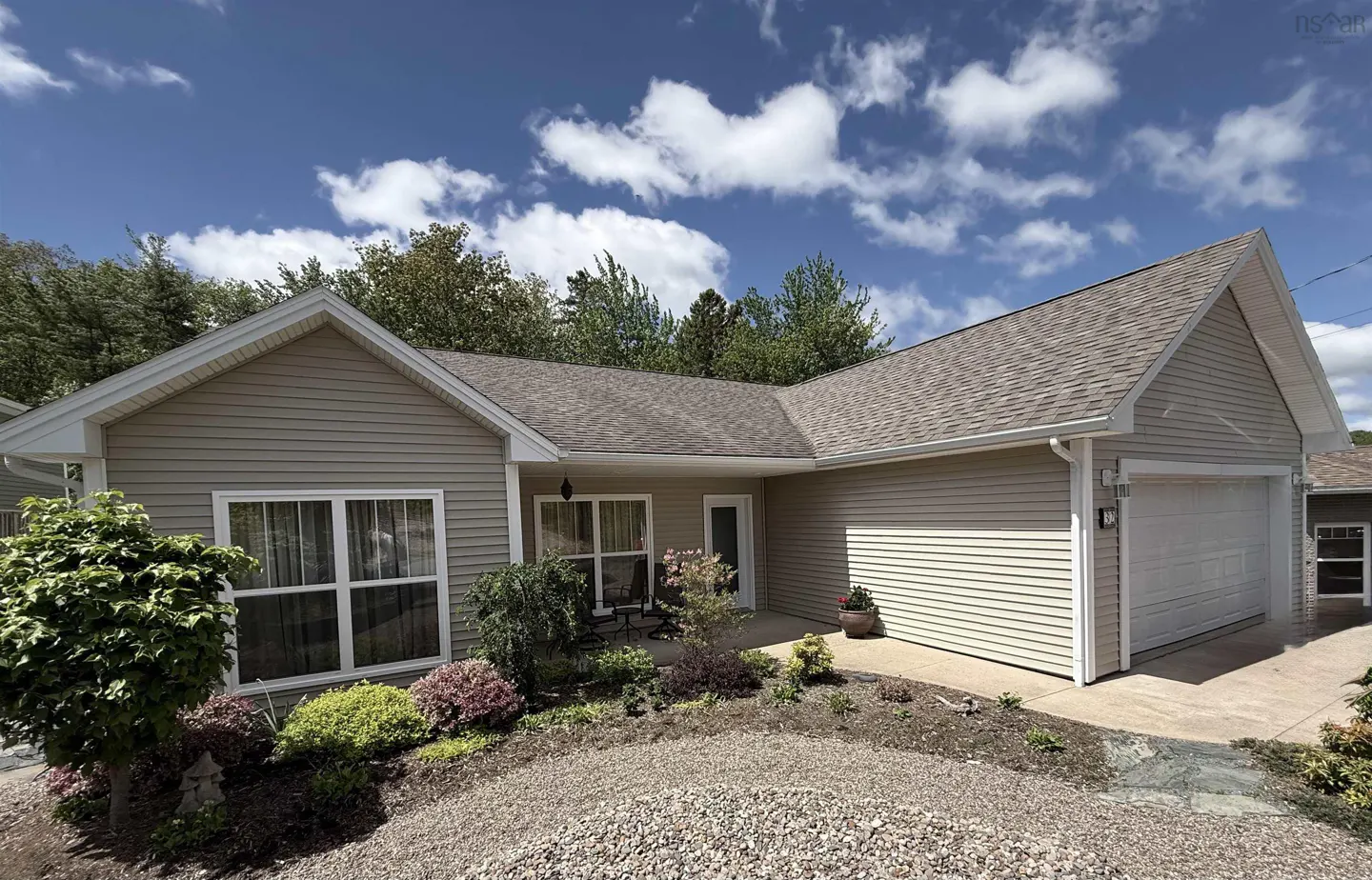 Single-story beige vinyl-sided house with a gray shingled roof, attached garage, and landscaped front yard under blue sky.