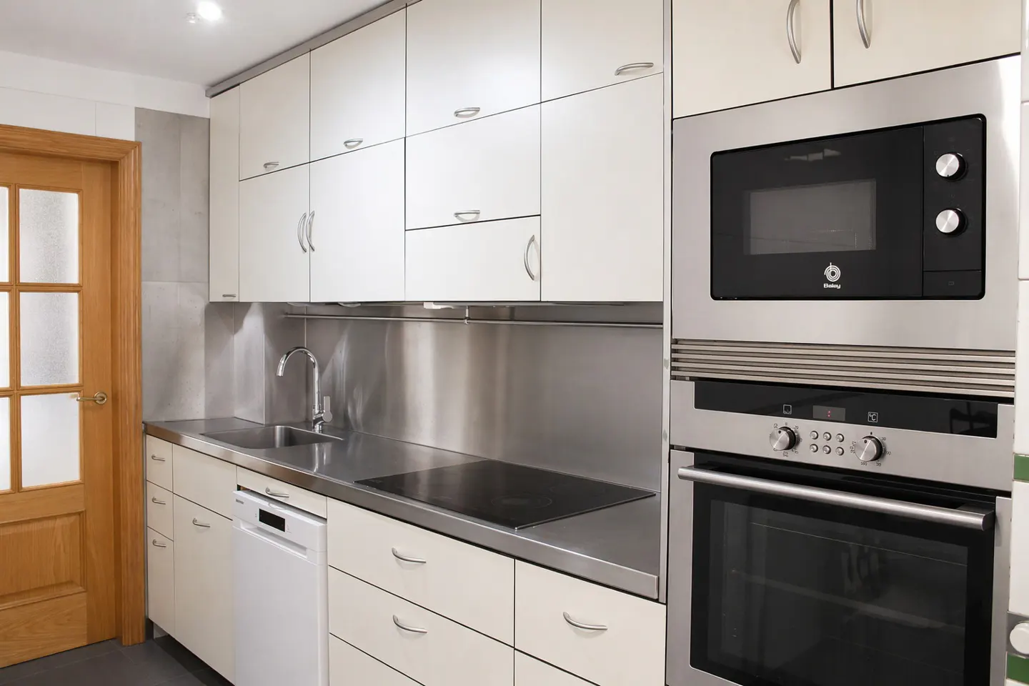 A modern kitchen with white cabinets, stainless steel countertops and backsplash, and built-in stainless steel microwave and oven.