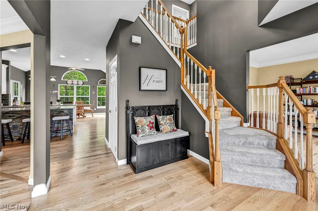 Foyer with gray walls, wood floors, and a staircase with wood railings and white spindles. A black bench with floral pillows sits beneath a framed "Home" print.
