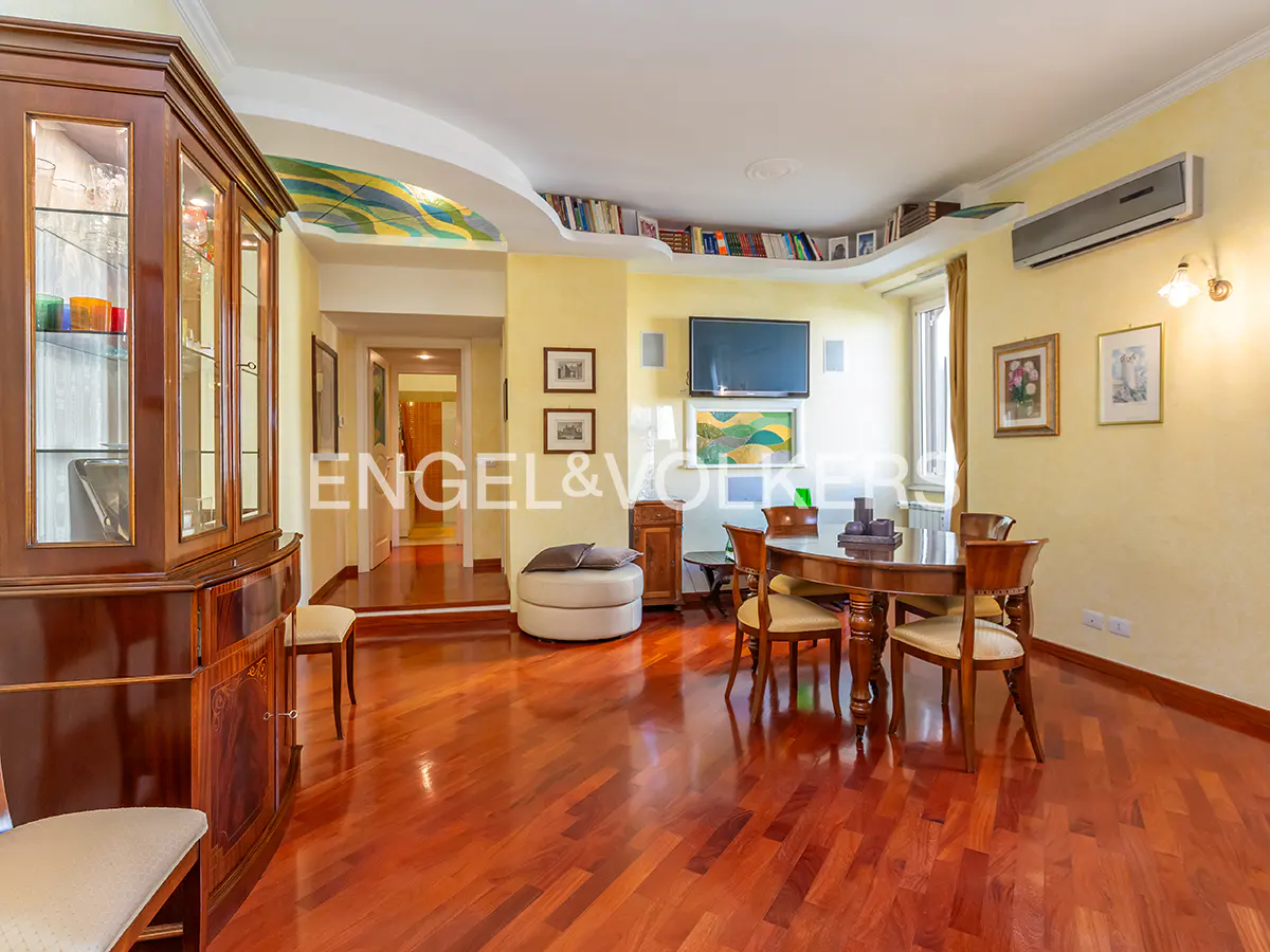 A living room with a wooden floor, a wooden cabinet, a round table with chairs, and a TV on the wall.