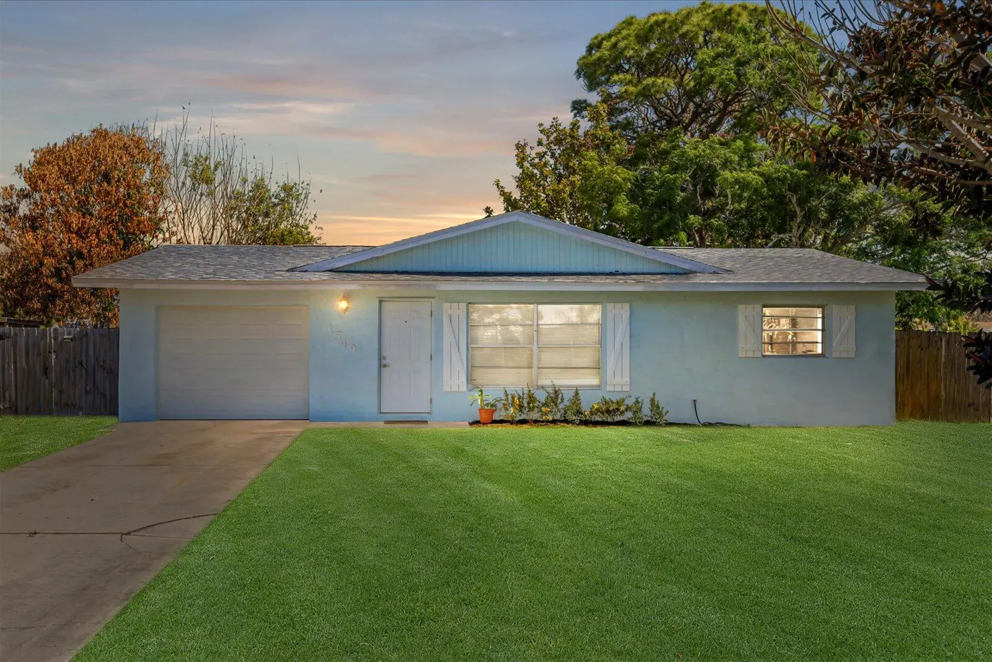 A light blue single-story house with a gray roof, white trim, and a green lawn at dusk.