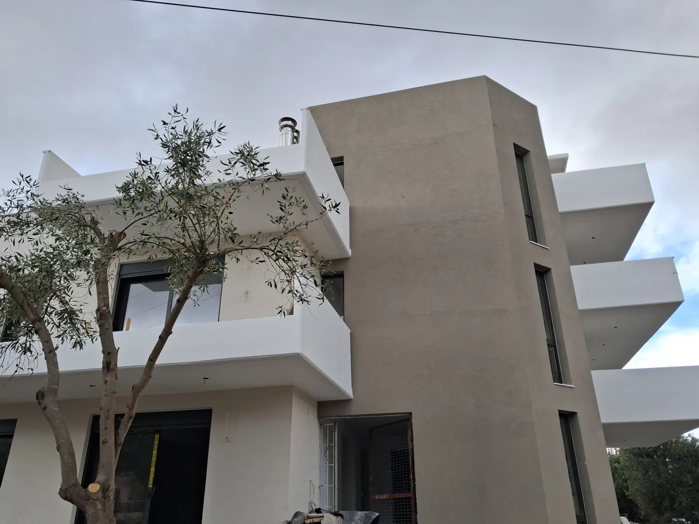 Modern apartment building with beige and white exterior, stacked balconies, and a small tree in the foreground.