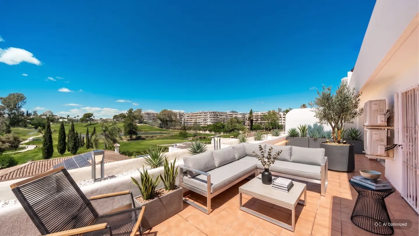 Outdoor patio with gray furniture, potted plants, and a view of a golf course under a bright blue sky.