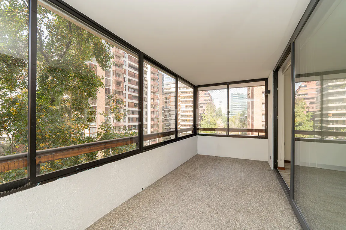 Enclosed sunroom with black framed windows overlooking city buildings and trees. The floor is speckled gray and the walls are white.