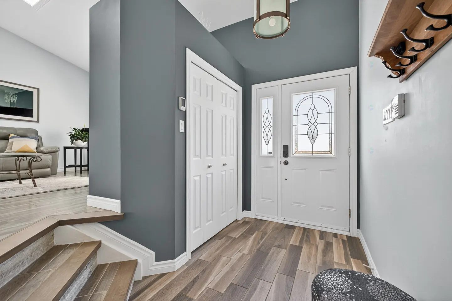 Entryway with wood-look tile floor, white front door with glass, closet, and coat rack on a light blue wall.