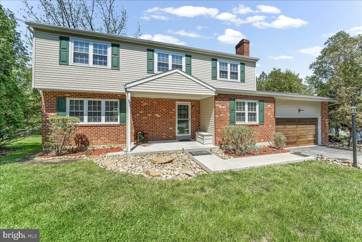 Two-story house with beige siding, brick accents, green shutters, and a chimney. Lawn in front.