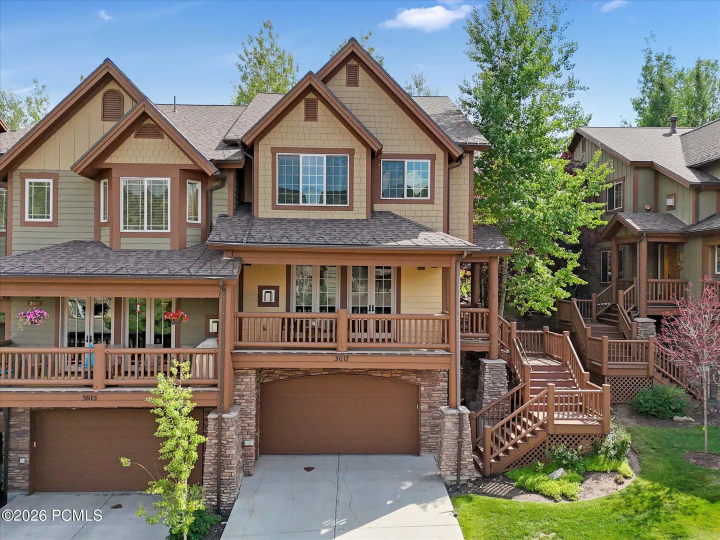 Exterior view of a multi-level townhouse with a brown garage door and stone accents. The house has a wooden porch and stairs.