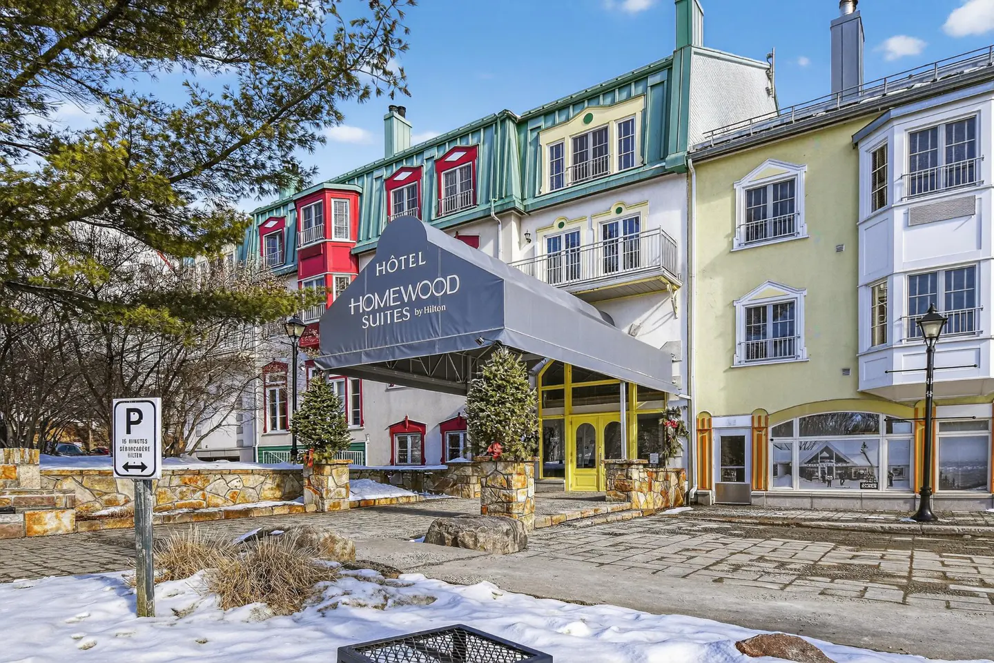 Hotel Homewood Suites entrance with a gray awning, yellow door, and colorful building facades on a snowy day.