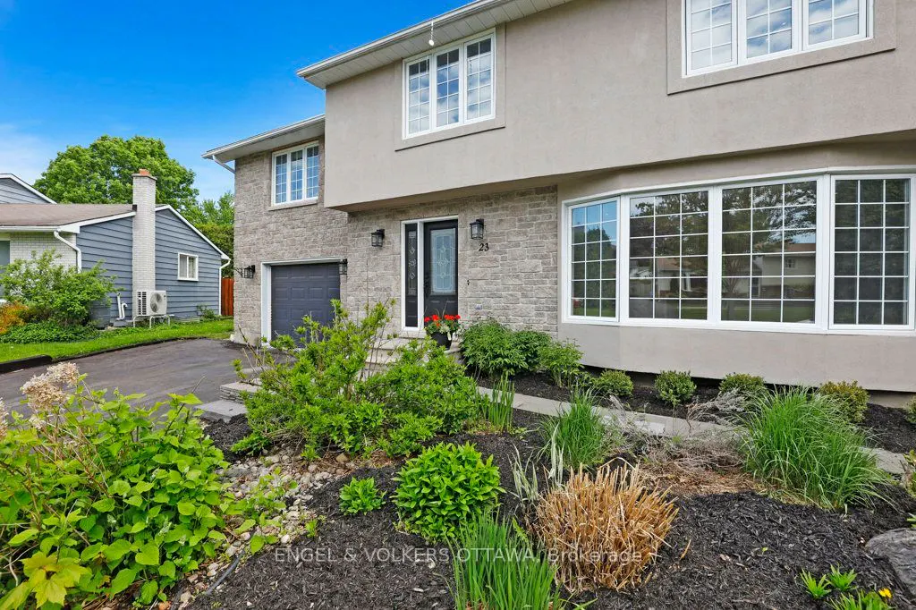 Two-story home with beige stucco, stone facade, large bay window, and a dark front door with a small garden in front.