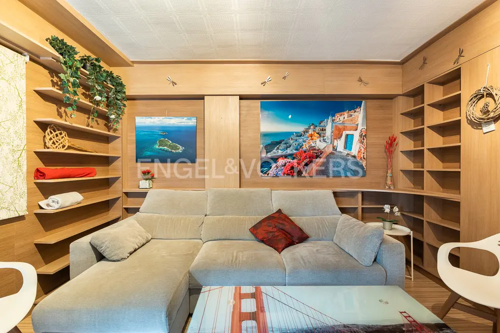 Living room with light wood paneling, built-in shelves, and a beige sectional sofa. Artwork and a Golden Gate Bridge-themed coffee table add color.