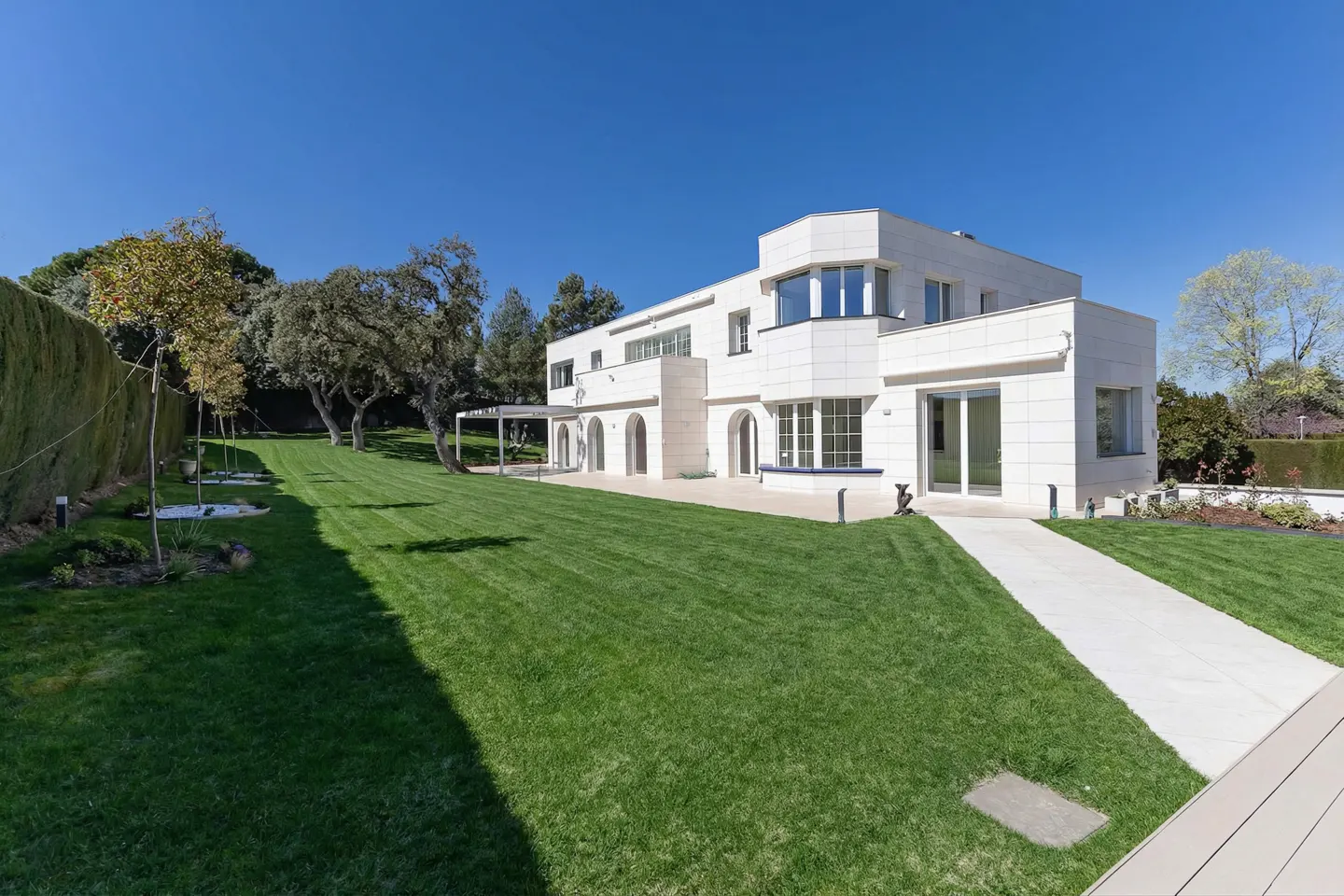 A modern, white, two-story house with a large green lawn and blue sky.