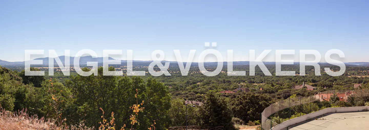 Panoramic view of a lush green landscape with mountains in the distance under a clear blue sky. The Engel & Völkers logo is superimposed on the image.