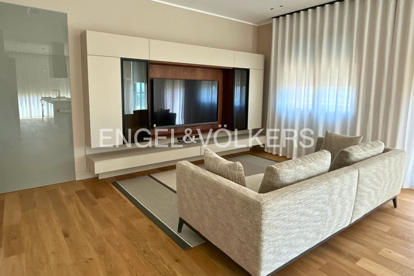 Modern living room with a beige sofa, hardwood floors, and a wall-mounted TV unit with wood accents and white cabinets.