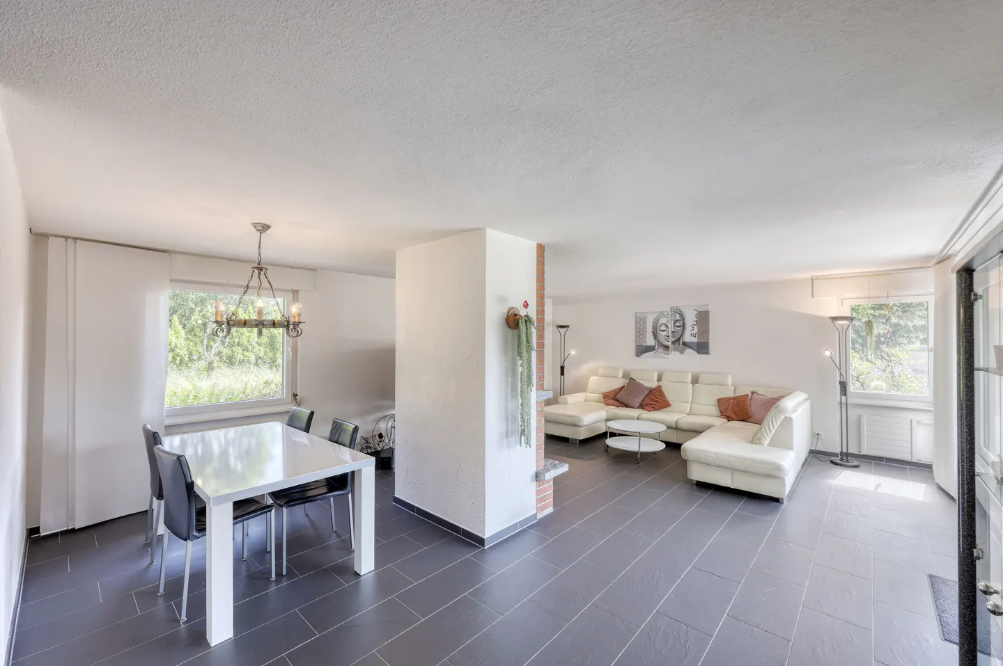 Open-concept living area with a white dining set, grey tile floors, and a large white sectional sofa in the lounge.