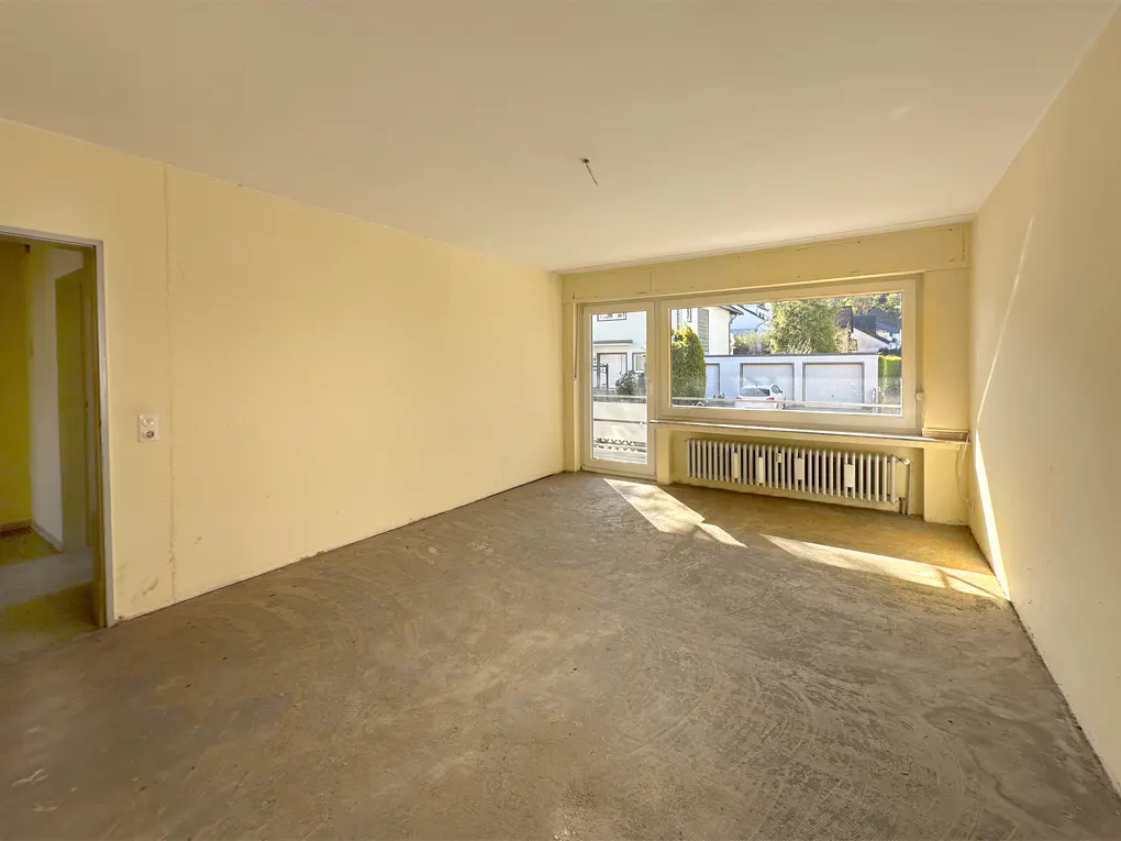 Empty room with yellow walls, concrete floor, and a large window showing a street view. A radiator sits beneath the window.