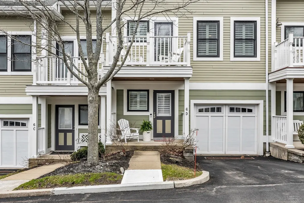 Exterior of three-story townhouses with sage green siding, white trim, and black doors. Balconies with white railings and white garage doors.