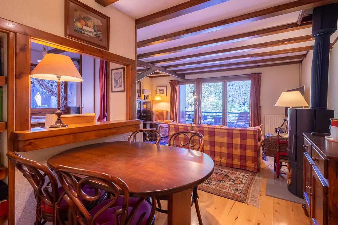 Rustic dining area with a round wooden table, chairs with purple cushions, and a cozy living room with a plaid sofa.