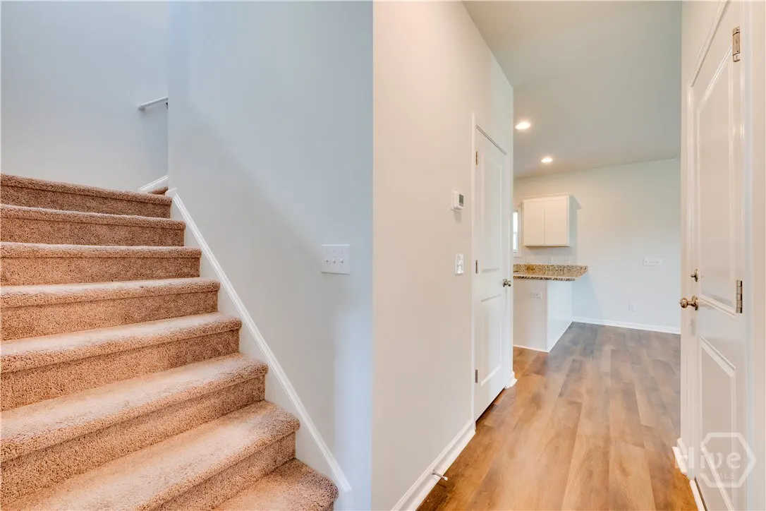 Interior view of a home featuring carpeted stairs, light gray walls, and wood floors leading to a kitchen area.