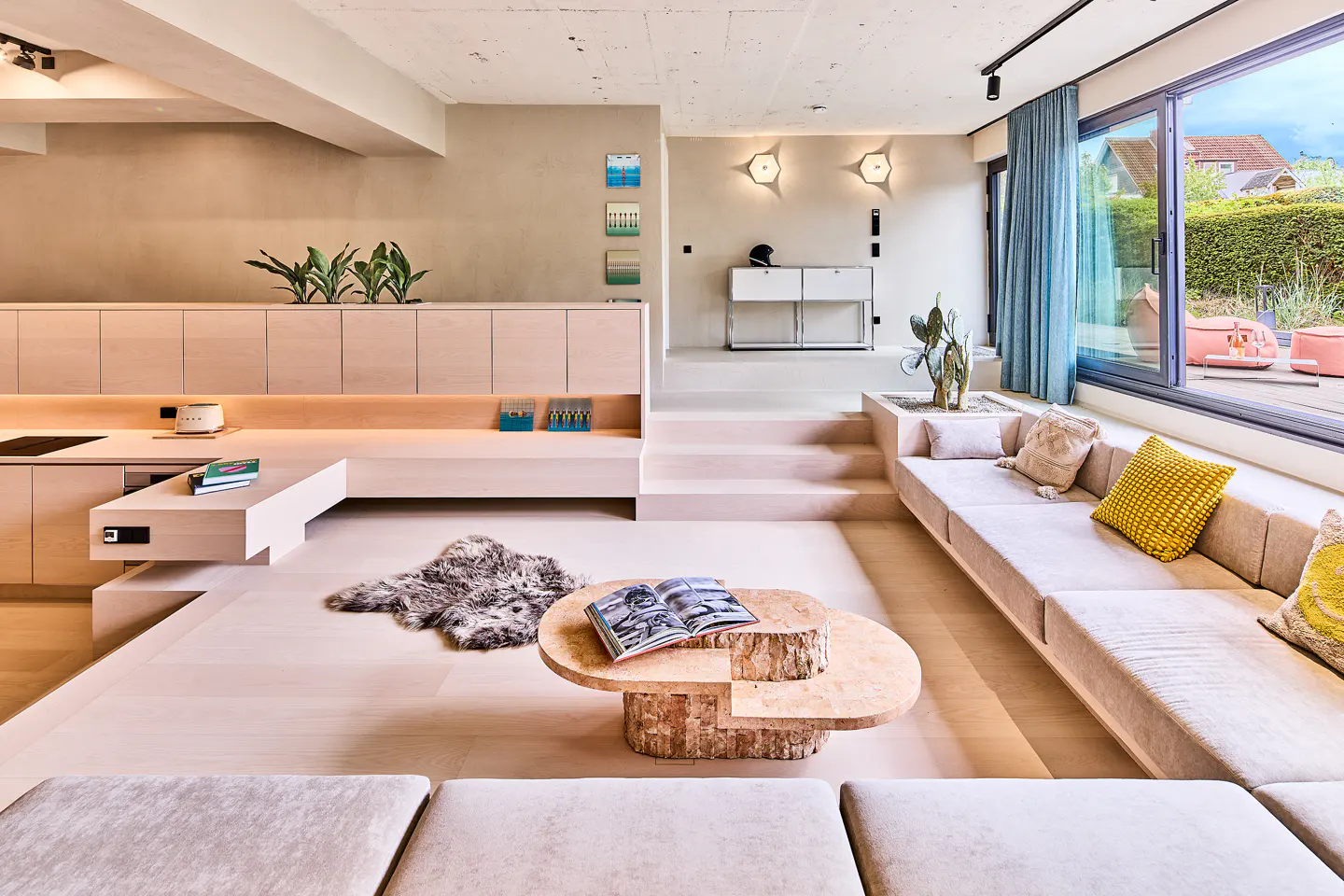 Modern sunken living room with light wood cabinetry, a long beige sofa, a unique wooden coffee table, and a fur rug.
