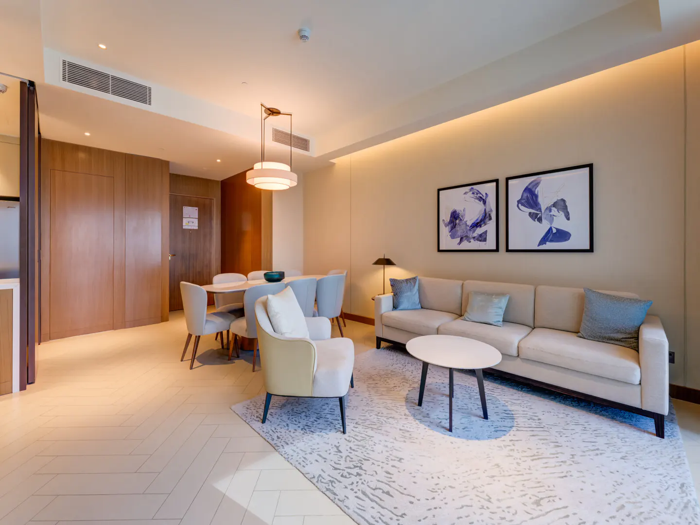 A modern living room with a beige sofa, blue pillows, a white coffee table, and two framed abstract art pieces.
