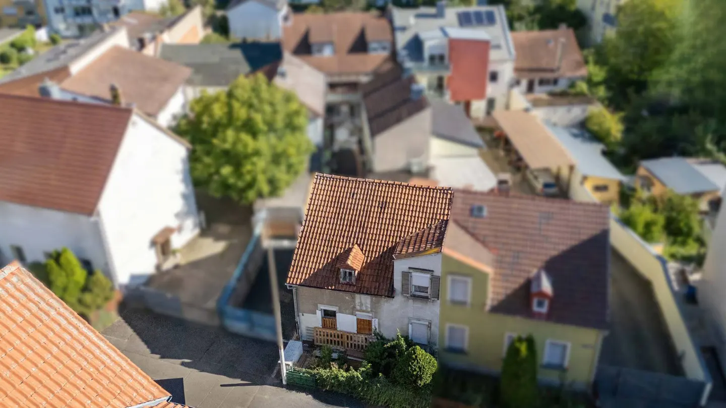 Aerial view of a quaint, two-story house with a red-tiled roof, surrounded by other homes and greenery.