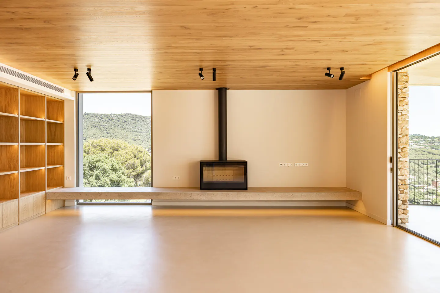 A modern living room with a black fireplace, light wood ceiling, and large windows with a view of green hills.