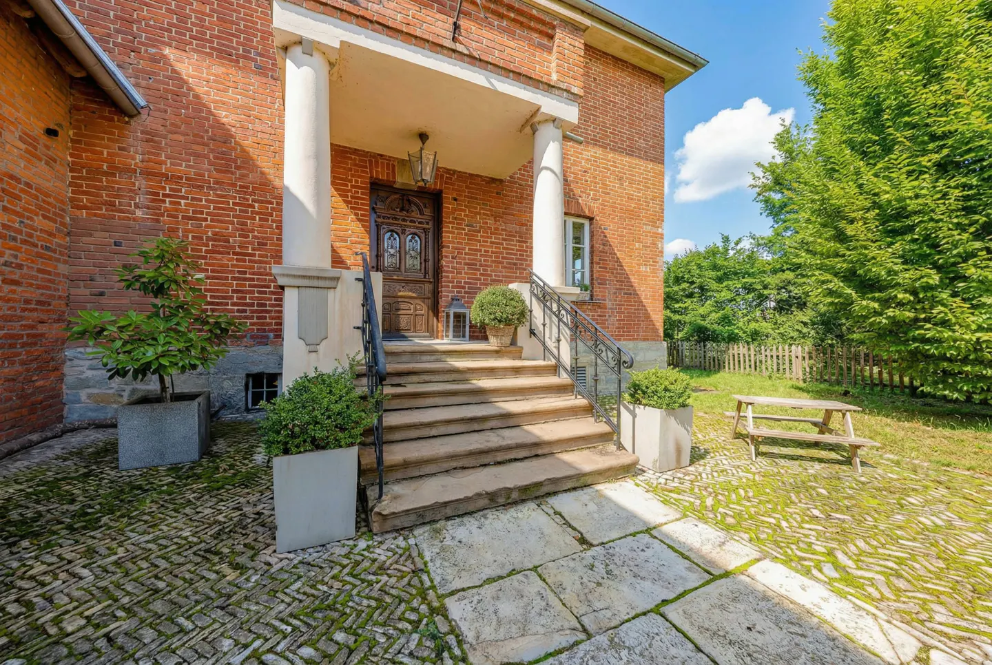 Brick house exterior with stone steps leading to a carved wooden door under a porch with white columns.