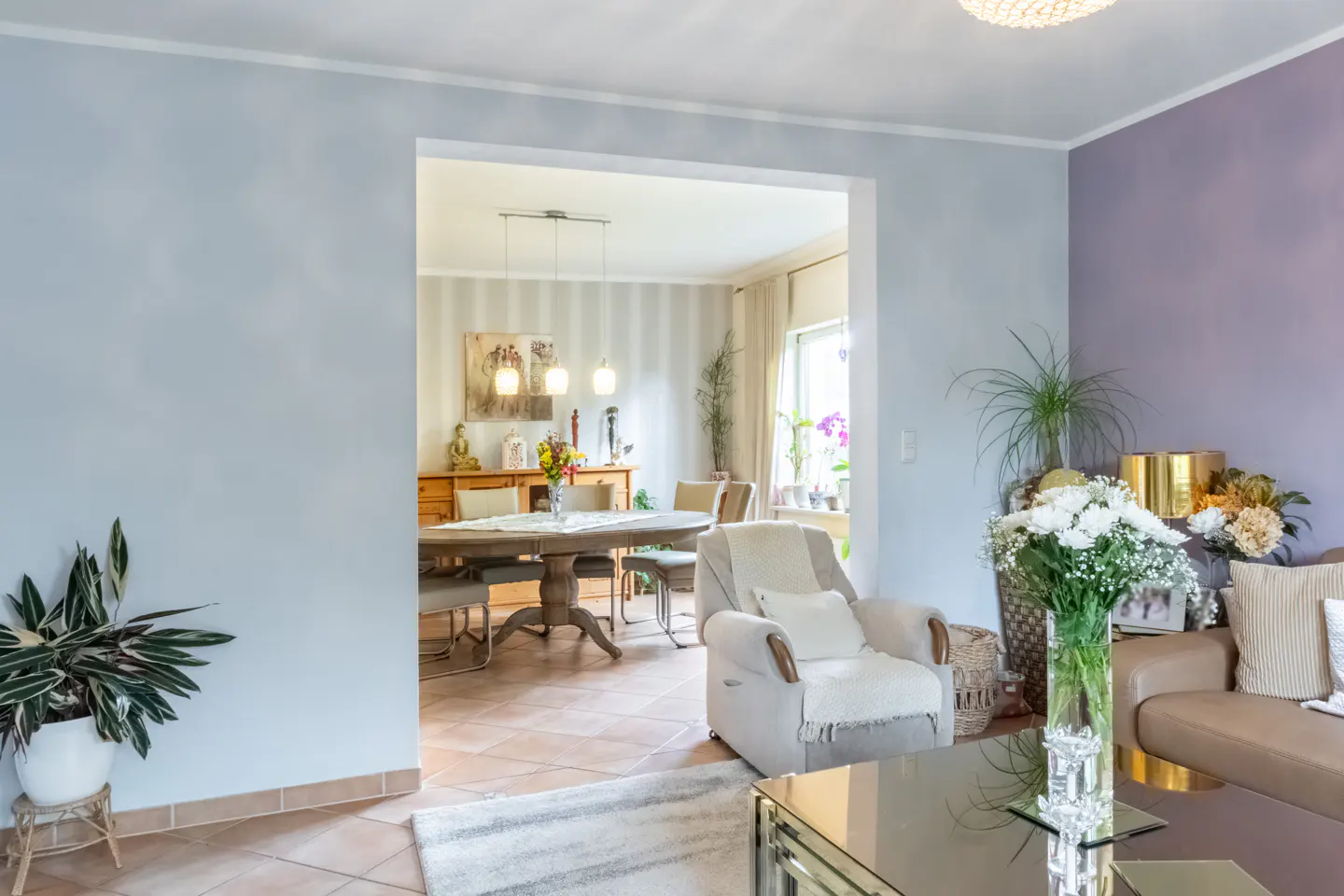 Living room with blue and purple walls, open to dining room with wood table and chairs. Flowers and plants add color.
