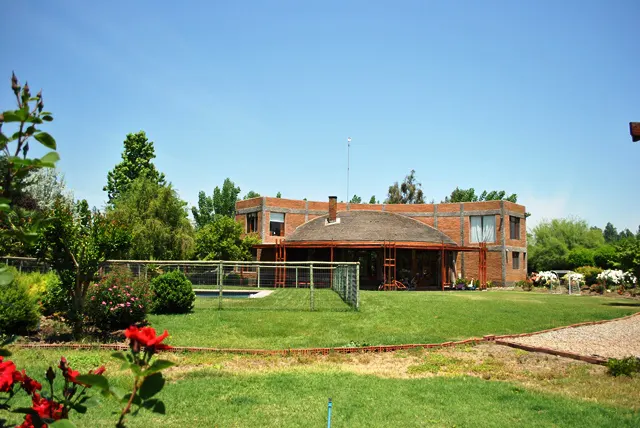 Brick house with a thatched roof and a covered patio, surrounded by a green lawn and trees under a blue sky.
