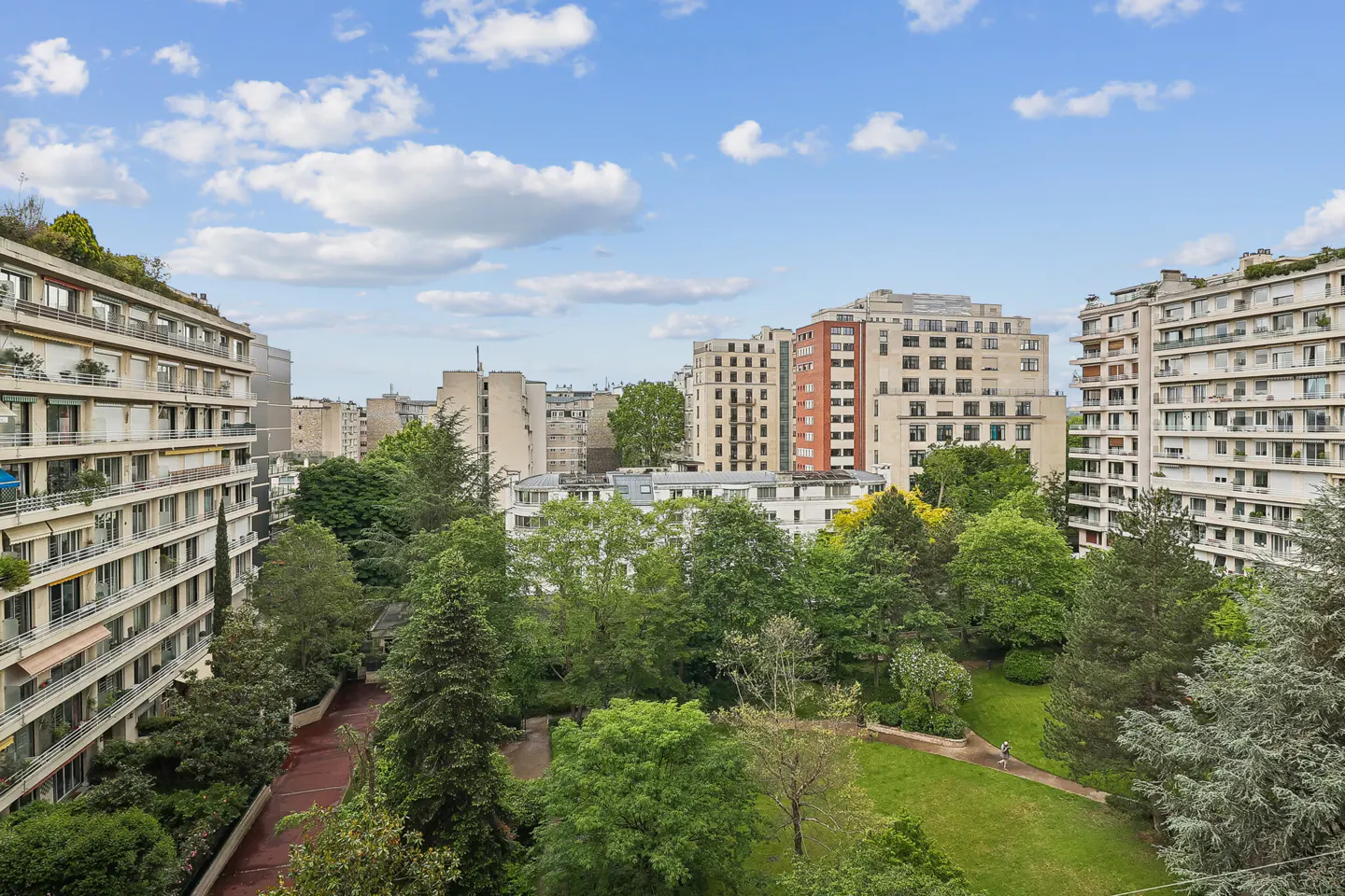 View of a park surrounded by apartment buildings under a blue, cloudy sky.