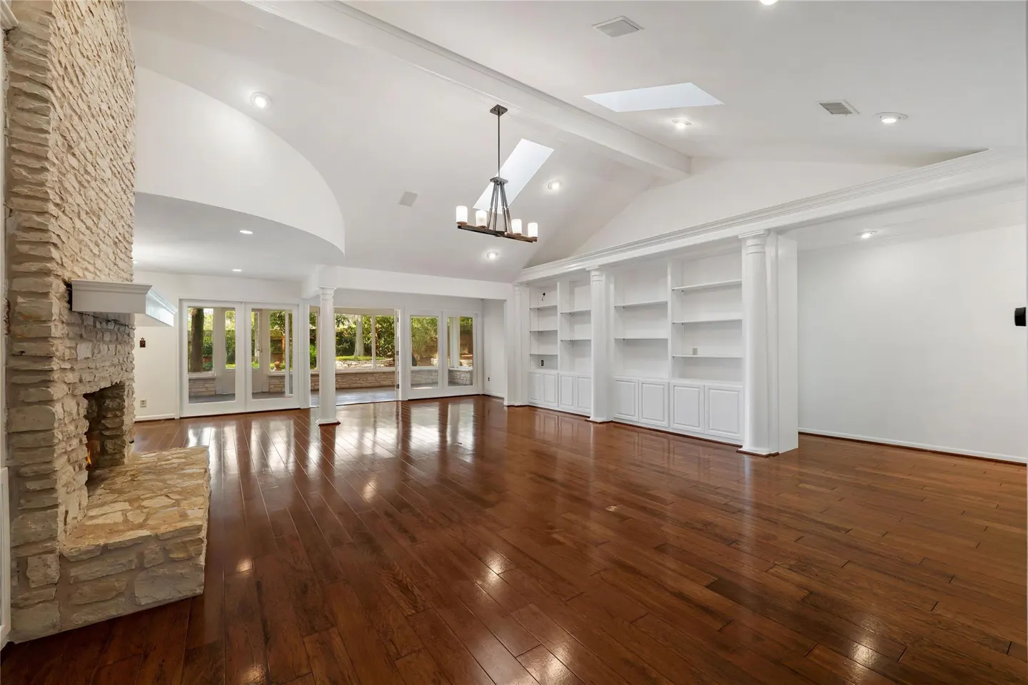 Bright, open living room with hardwood floors, stone fireplace, white built-in shelves, and glass doors to a patio.