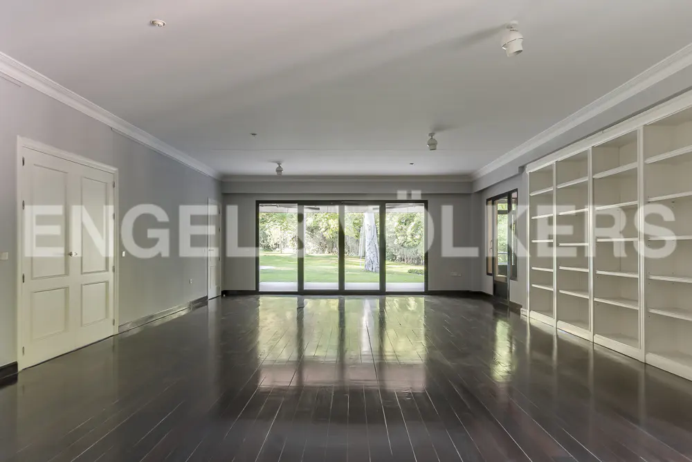 An empty room with dark wood floors, white trim, and a wall of built-in bookshelves. Sliding glass doors lead to a green lawn.