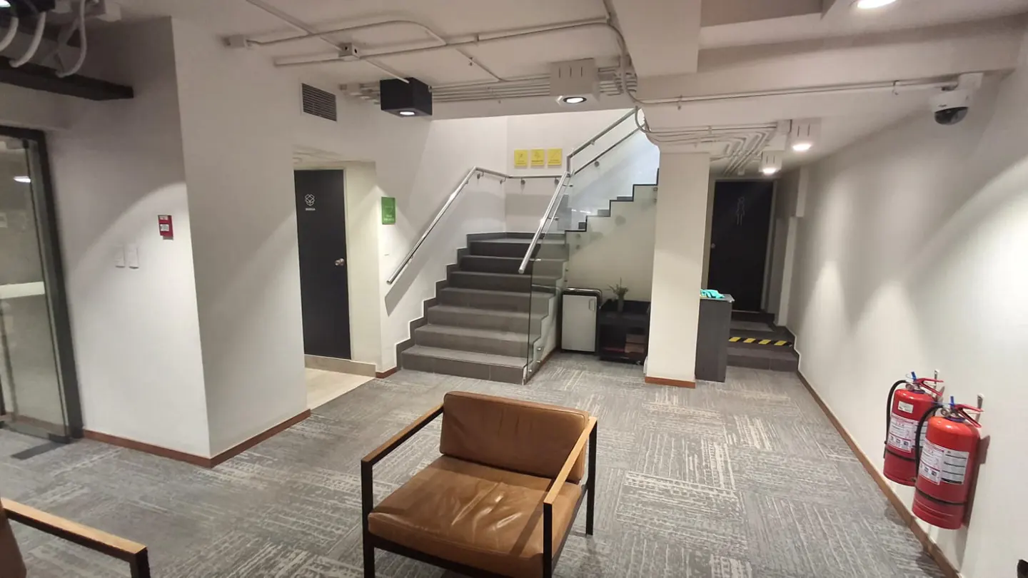 Interior view of a building lobby with a brown leather chair, stairs, and two red fire extinguishers.