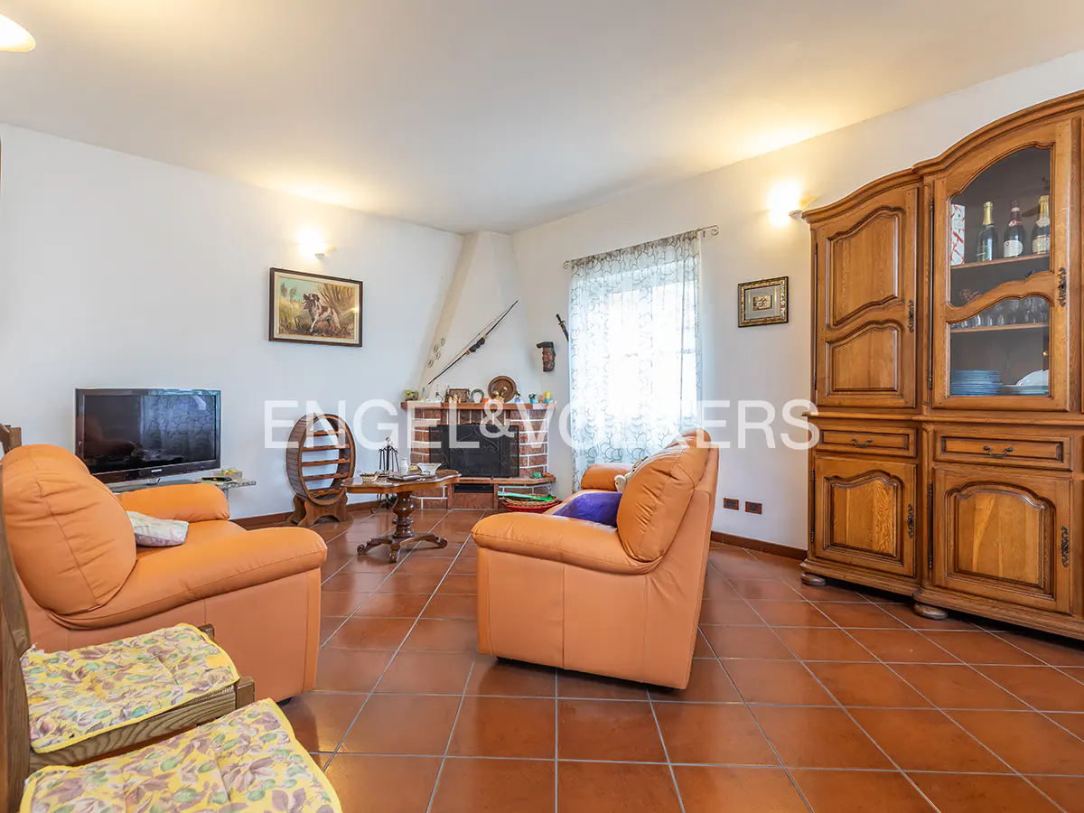A living room with orange armchairs, a brick fireplace, and a wooden cabinet. The floor is tiled in terracotta.