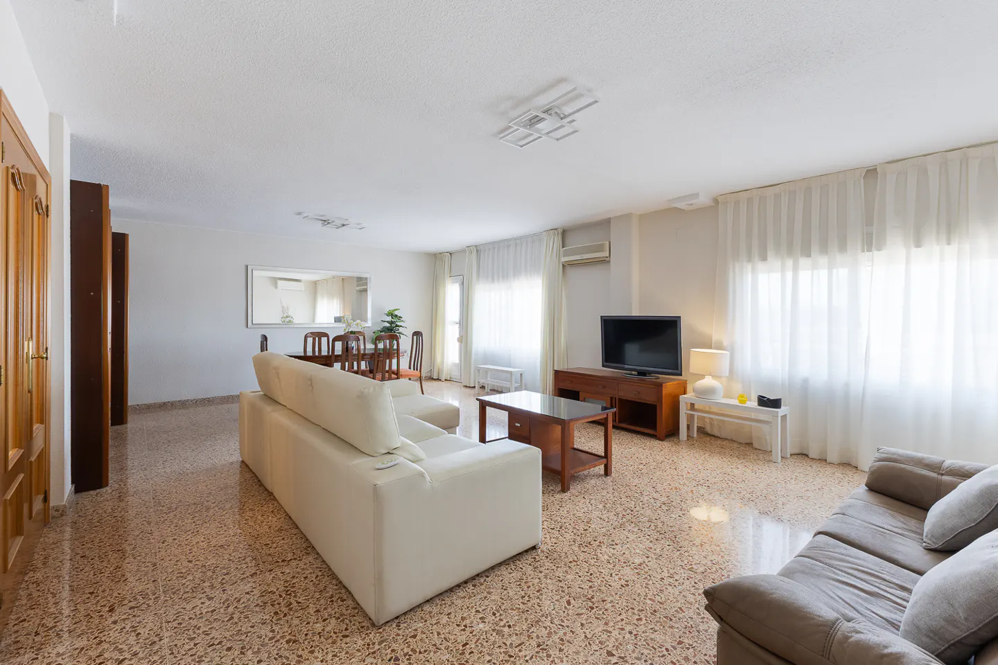 Bright living room with white sofa, brown sofa, TV, dining table, and terrazzo floor.