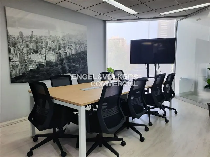Conference room with a light wood table, black chairs, and a large black and white city print on the wall. A large screen is on the right.