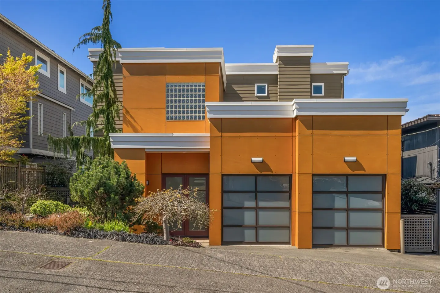 Modern two-story house with orange siding, white trim, and two glass garage doors on a sunny day.