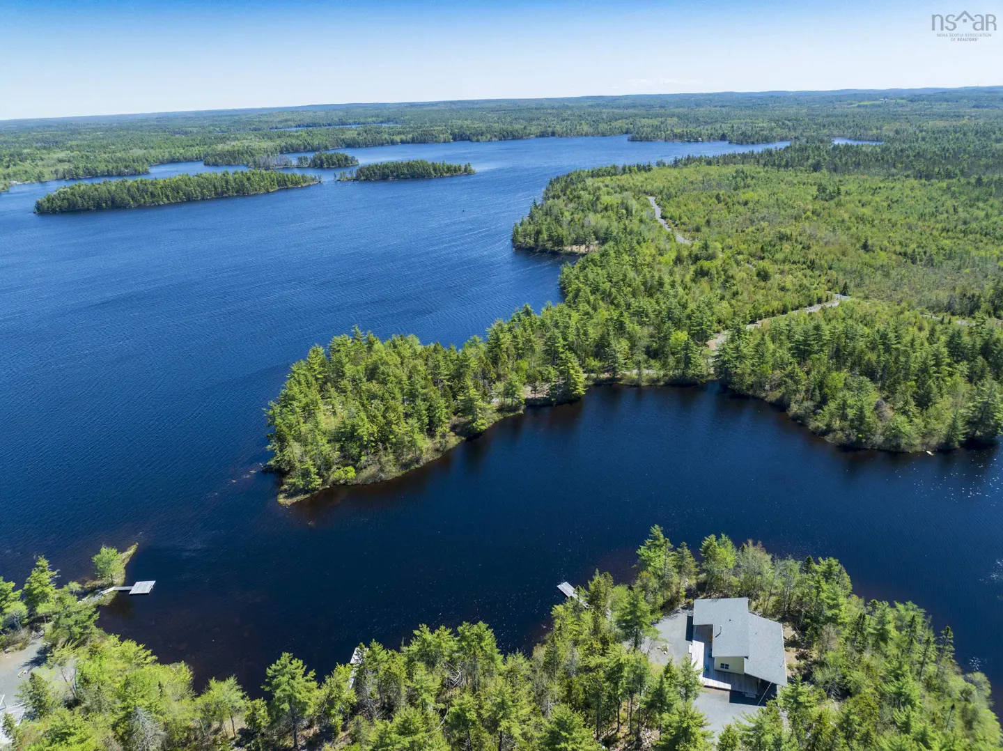 Aerial view of a blue lake with green forested islands and a house on a peninsula.