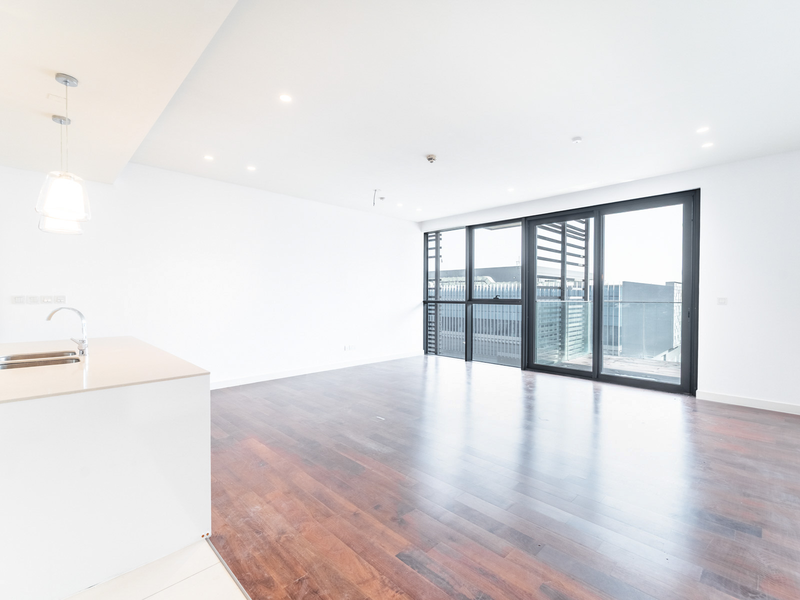 Bright, modern open-plan living area with dark wood floors, white walls, and floor-to-ceiling glass doors to a balcony.