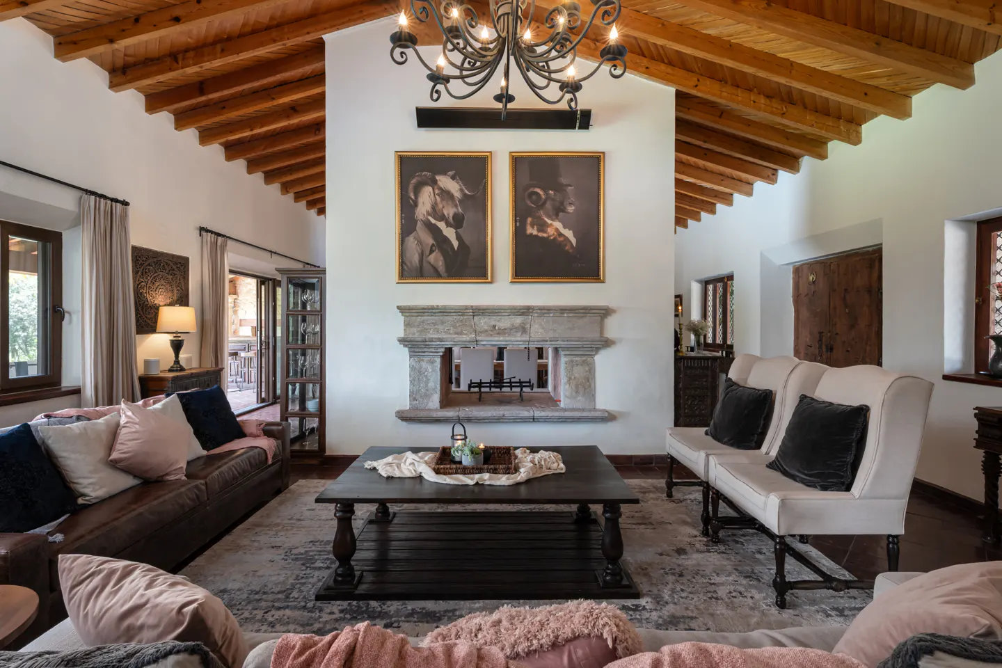 Living room with wood-beamed ceiling, stone fireplace, and dark wood furniture. Two framed animal portraits hang above the fireplace.