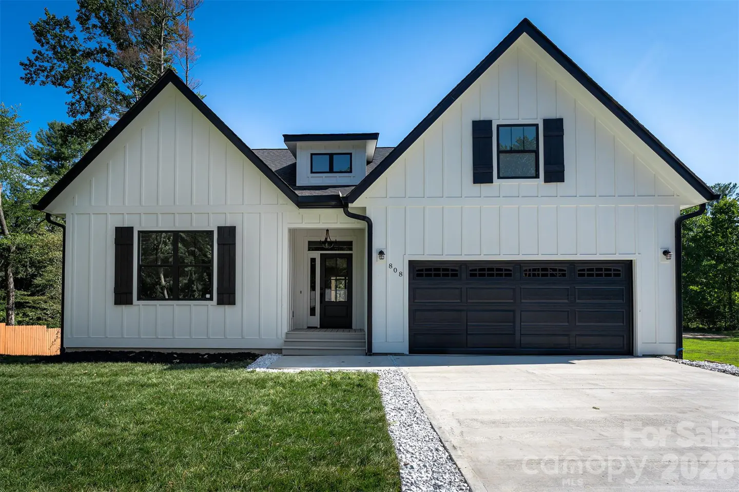 A modern farmhouse with white siding, black trim, and a two-car garage under a clear blue sky.