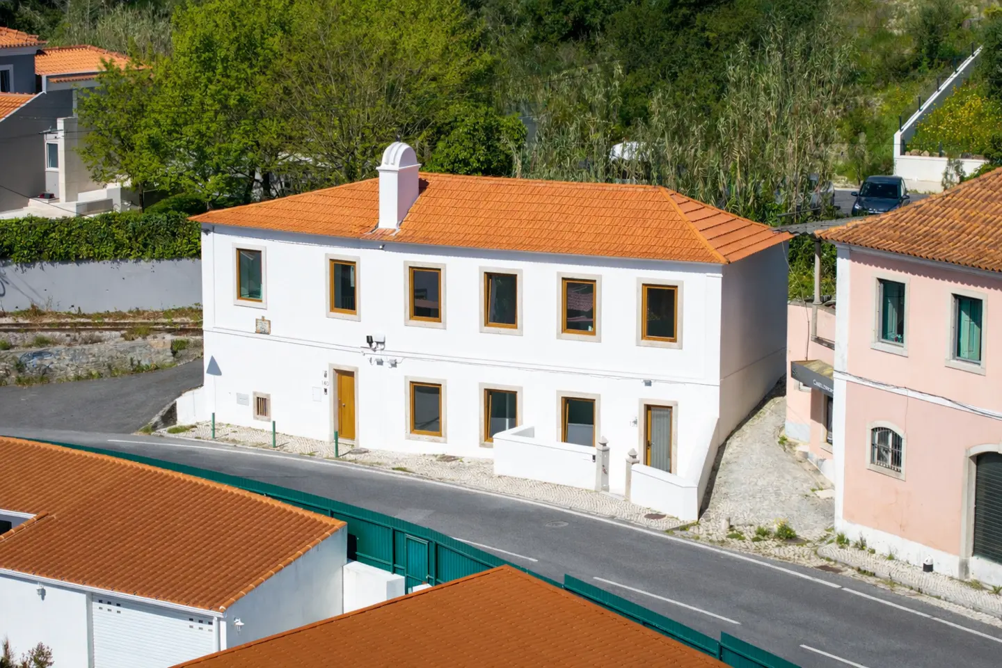 A white two-story building with an orange tile roof and a yellow door. The building is next to a road.
