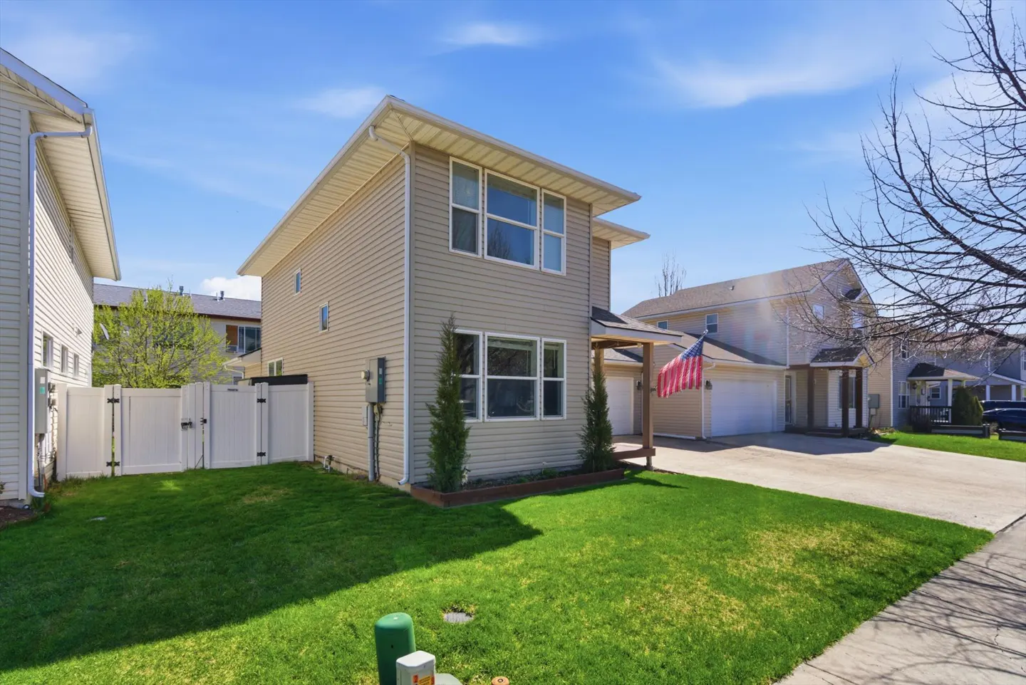 Tan two-story house with white trim, green lawn, and American flag on the porch.