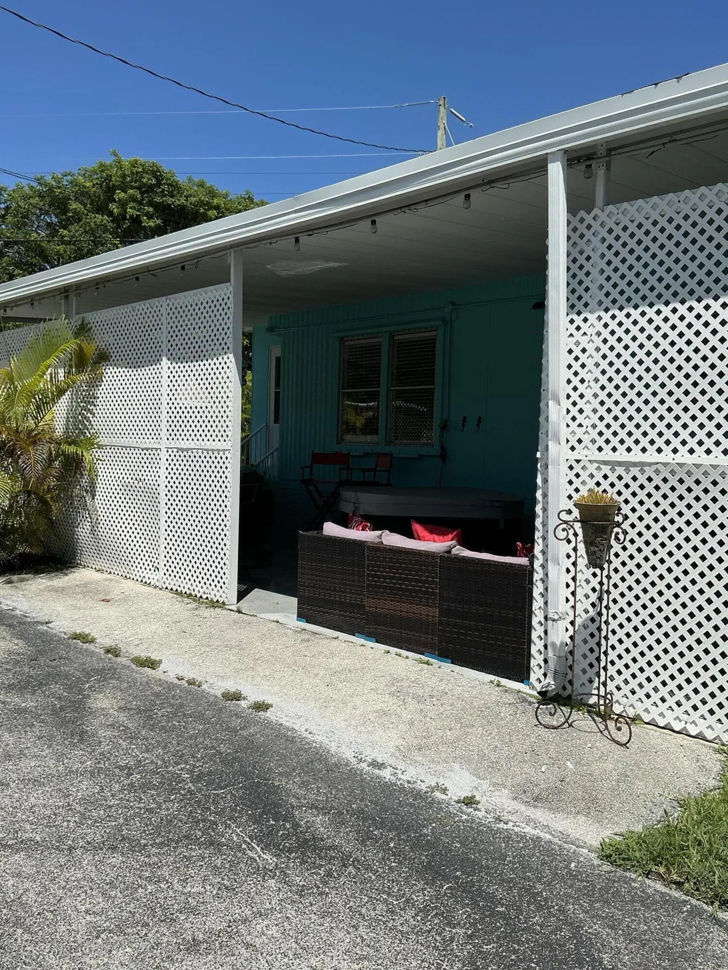 A turquoise house with a covered patio, white lattice privacy screens, dark wicker furniture, and a potted plant.