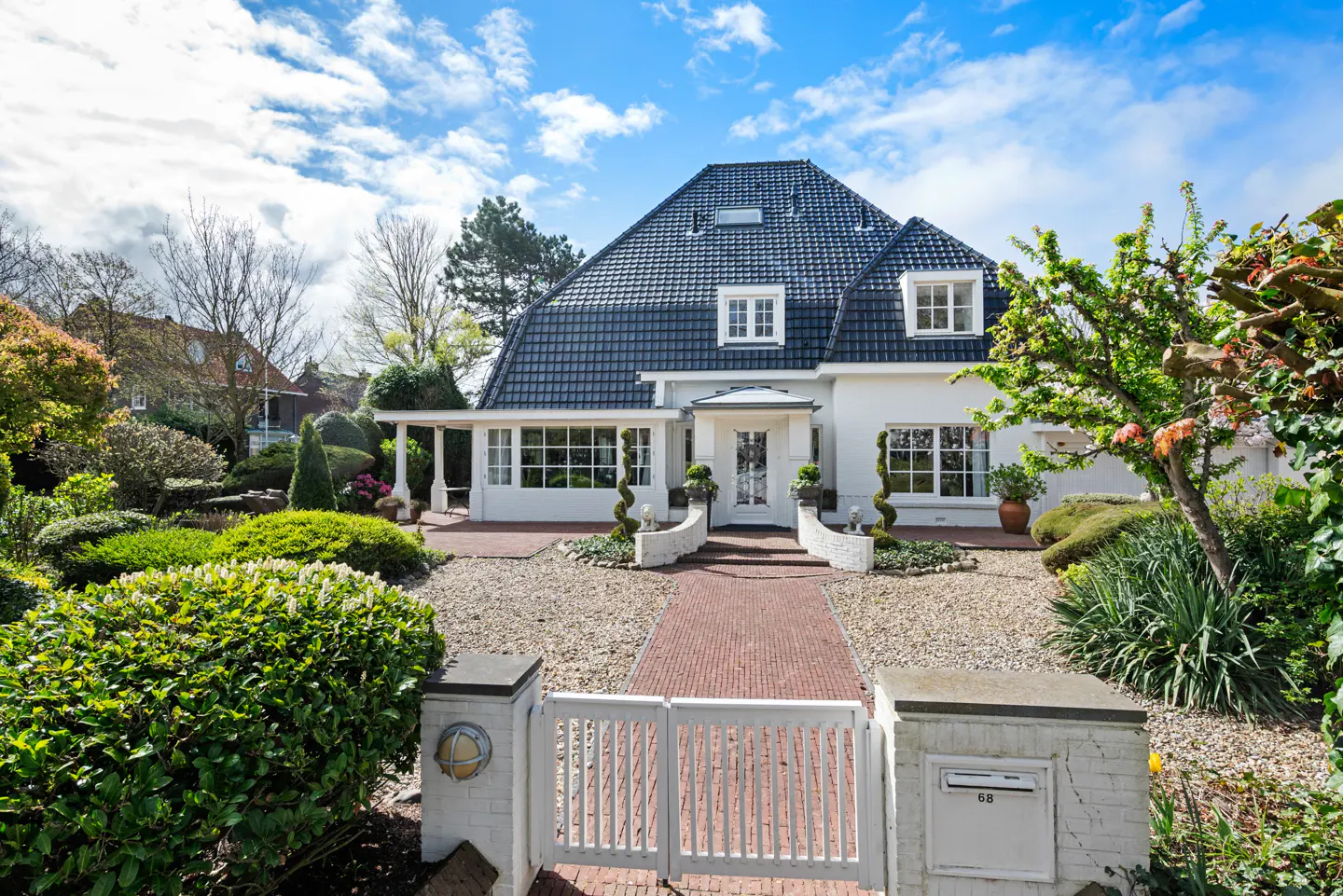 Exterior of a white house with a dark roof, brick path, and white gate.