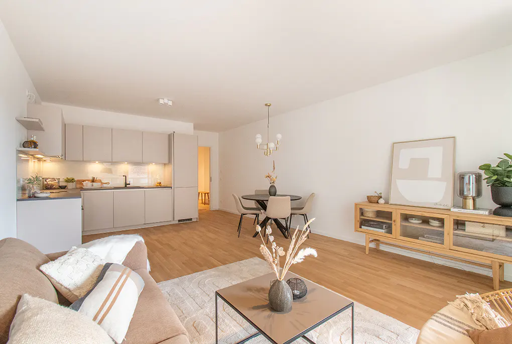 Modern open-plan living room with beige kitchen, dining area, and cozy seating space featuring light wood floors.