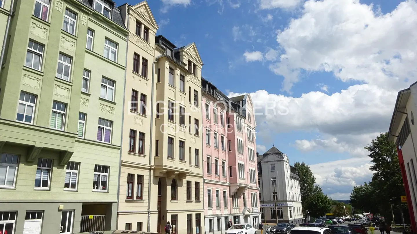 A row of colorful historic apartment buildings in shades of green, cream, and pink under a bright blue sky with clouds.