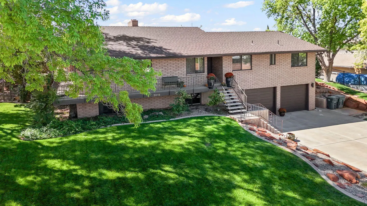 Two-story brick house with a brown roof, green lawn, and a stairway leading to the front door.