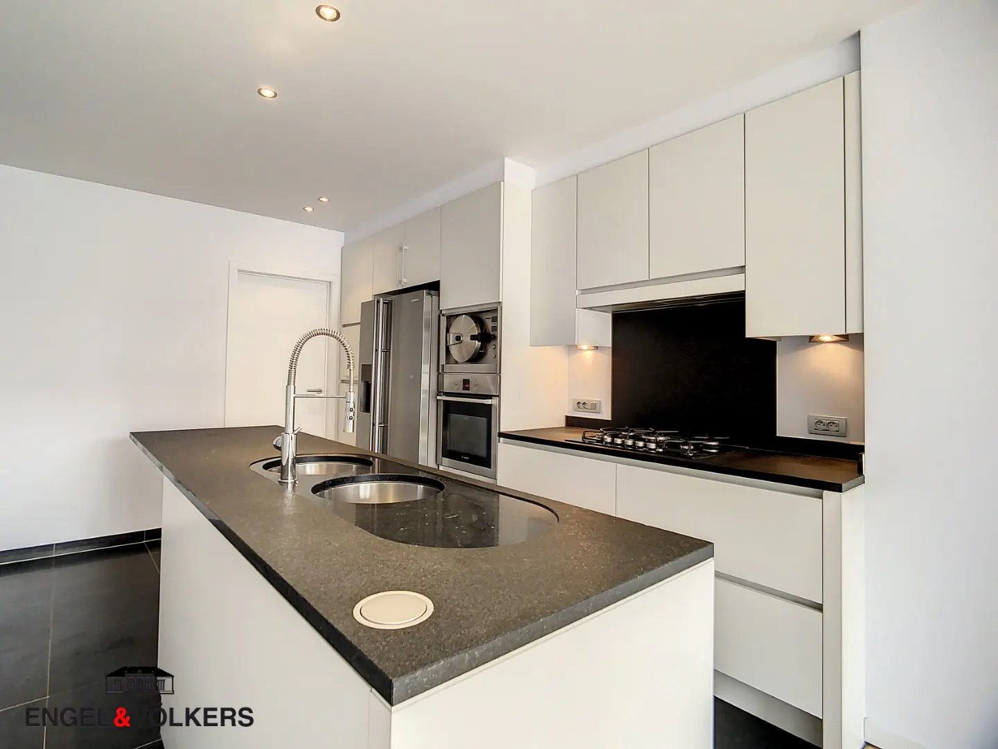 A modern kitchen with white cabinets, stainless steel appliances, and a dark countertop island with a sink.