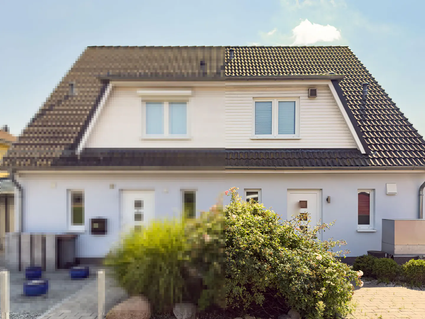 Two-story duplex with a brown tile roof, white siding, and green bushes in front. The left side of the image is pixelated.